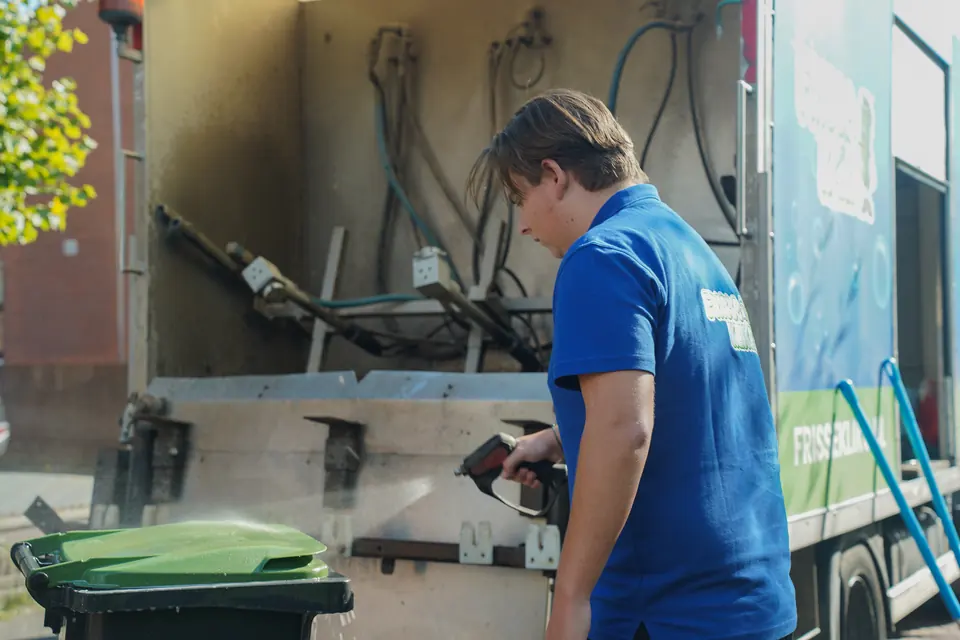 Medewerker reinigt een groen containerdeksel met een spuitlans.